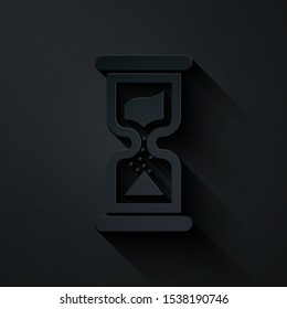 Paper cut Old hourglass with flowing sand icon isolated on black background. Sand clock sign. Business and time management concept. Paper art style. Vector Illustration