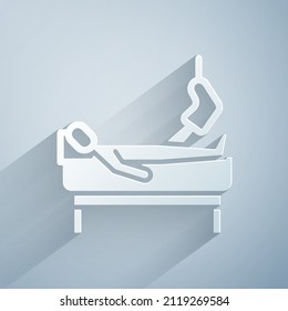 Paper cut Patient with broken leg is in the hospital icon isolated on grey background. Hospitalization of the patient. Sick man in bed. Paper art style. Vector