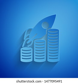 Paper cut Rocket flying up on coins growth chart icon isolated on blue background. Graph that shows increase in sales. Paper art style. Vector Illustration