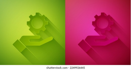 Paper cut Settings in the hand icon isolated on green and pink background. Paper art style. Vector Illustration