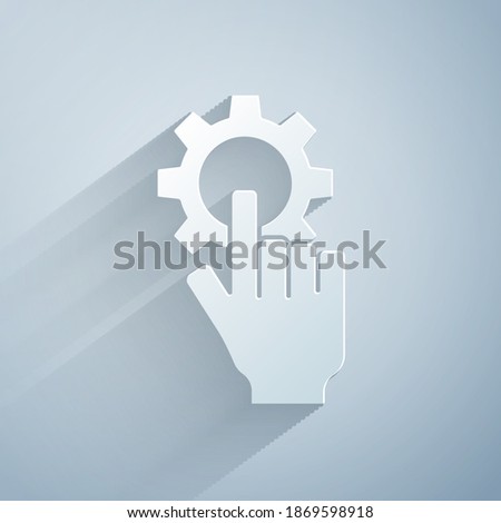 Paper cut Settings in the hand icon isolated on grey background. Paper art style. Vector