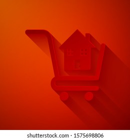 Paper cut Shopping cart with house icon isolated on red background. Buy house concept. Home loan concept, rent, buying a property. Paper art style. Vector Illustration