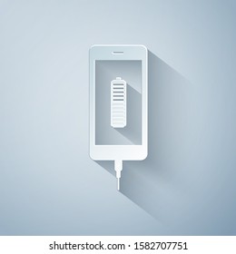 Paper cut Smartphone battery charge icon isolated on grey background. Phone with a low battery charge and with USB connection. Paper art style. Vector Illustration