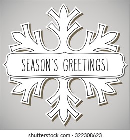 Paper cut snowflake and a frame with hand written season's greetings over light grey background.