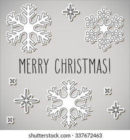 Paper cut snowflakes and hand written Christmas greetings over gray background.