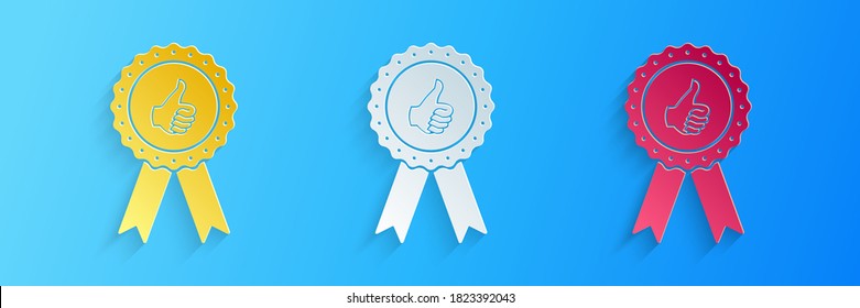 Paper cut Thumbs up on medal badge with ribbons icon isolated on blue background. Paper art style. Vector.