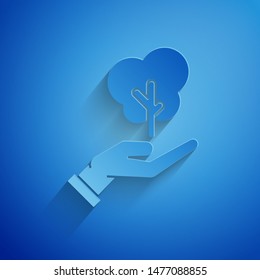 Paper cut Tree in hand of environmental protection icon isolated on blue background. Seed and seedling. Planting sapling. Ecology concept. Paper art style. Vector Illustration