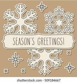 Paper snowflakes and a frame with hand written season's greetings over vintage brown background.