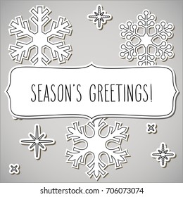Paper snowflakes and a frame with hand written season's greetings over gray background.