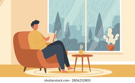Peaceful man reading a book while relaxing in a cozy armchair next to a window on a rainy day in autumn or winter.