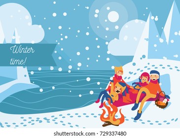 People having winter picnic with bonfire, food and fruits on a lake shore