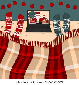 People are on the bed with knitted red and blue socks. They are watching to laptop, it is video call with Santa Claus with gifts, who is waving hand in Christmas time
