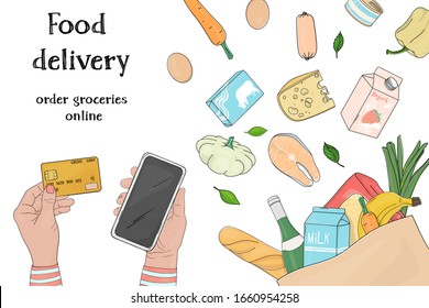 Person orders food online by phone and pays with a credit card. Grocery, vegetables and fruits in a paper bag on a white background. Food delivery from the supermarket. Space for your text. Template.