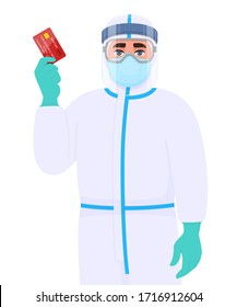 Person in safety protection suit, medical mask, glasses and face shield showing credit, debit, ATM card. Doctor or physician holding banking card. Surgeon wearing personal protective equipment (PPE).