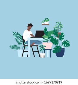 A person staying home working on the laptop in the kitchen. A room full of plants.