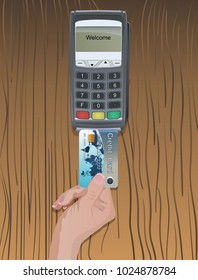 A person's hand inserts a credit card into the chip reader of the terminal on a table with a wooden texture