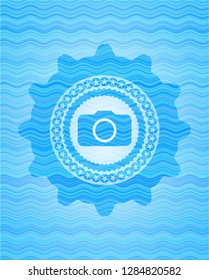 photo camera icon inside light blue water wave style emblem.