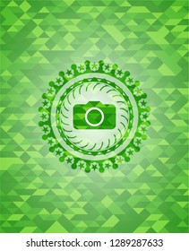 photo camera icon inside realistic green emblem. Mosaic background