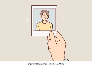 Photo of teenager boy in hand of father or mother for concept of nostalgia for times gone by. Sentimental man looks at photo of little laughing boy, looking back at times when son was little.