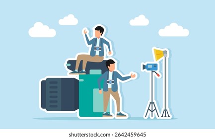 Photographer sitting on camera while another stands near camera standing lamp and standing camera illustration of being ready for a photo session