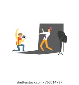 Photographer sitting on his knee and holding camera in hand. Young man model posing on black backdrop. Shooting photo in professional studio. Flat vector