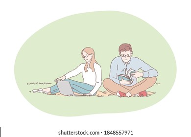 Picnic, relaxing, resting in park with book and laptop concept. Young happy couple sitting on blanket on grass in public park and relaxing with book and laptop during lunch break or weekend together