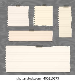 Pieces of torn brown lined note paper are stuck on gray wooden wall or board