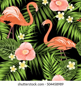 Pink flamingos in palm tree leaves with exotic plumeria frangipani and camellia flowers. Jungle rain forest concept seamless pattern on black background.