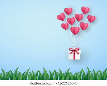 Pink origami hot air balloon in heart shape with gift box flying on the sky over the green meadow in Valentine's day with mini hearts on blue background. Vector art design in paper cut pop up style. 