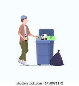 poor man beggar holding bottle of alcohol tramp searching food and clothes in trash can on street homeless jobless unemployment poverty concept white background full length