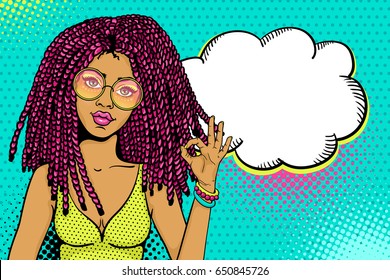 Pop art female face. Sexy african american hippie woman with pink dreadlocks in round glasses shows okay sign and empty speech bubble. Vector colorful background in pop art retro comic style.