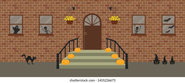 Porch, decorated for Halloween. Front Porch Halloween Decorations. There are pumpkins, pots of chrysanthemums and black cat on a brick facade background. There are bats and skeletons in the windows