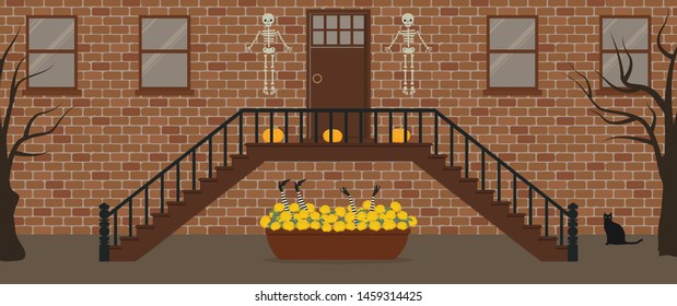 Porch, decorated for Halloween. Front Porch Halloween Decorations. There are skeletons, pumpkins, black cat and a pot of chrysanthemums and witch's feet and hands on the background of the brick facade