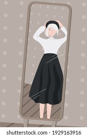 Portrait of a cute young French lady with short haircut wearing a long skirt and a light blouse trying on a beret in front of the mirror in the fitting room of a fashionable clothes shop