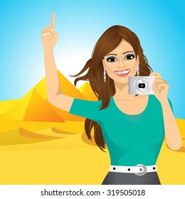 portrait of young pretty woman woman taking a picture and pointing up against Egyptian pyramids
