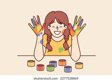 Positive girl with face and palms smeared with multi-colored paint smiles, wanting to become artist or designer. Smiling girl with gouache or watercolor on hands rejoices at school art lesson 