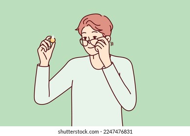 Positive man examines gold coin or piece of jewelry and lowers glasses from eyes to view rare exhibit. Guy is fond of numismatics and collecting coins from precious metals. Flat vector design 