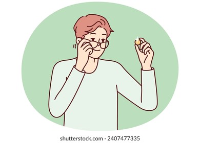 Positive man examines gold coin or piece of jewelry and lowers glasses from eyes to view rare exhibit. Guy is fond of numismatics and collecting coins from precious metals. Flat vector design