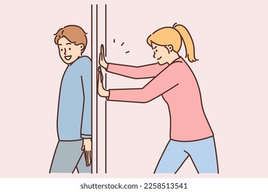 Positive man hides behind door and blocks passage preventing girlfriend from passing or arranging prank to entertain each other. Girl and guy have fun together during weekend, arranging playful pranks