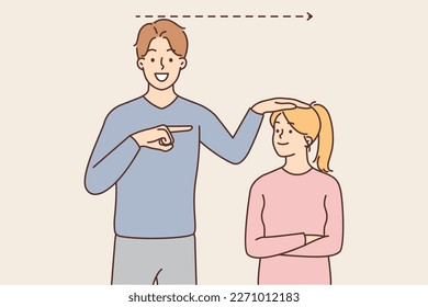 Positive man showing growth of little daughter and pointing finger at teen girl rejoicing in growing up process. Satisfied father measures growth of teenager girl for concept of happy childhood