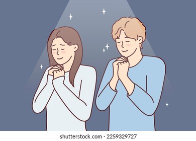 Positive man and woman praying asking god for happy marriage. Young couple stand with eyes closed and clasping palms in front of chest together performs religious ritual