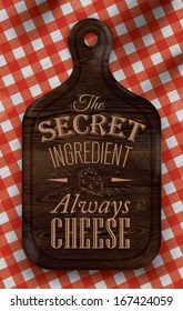 Poster with bread cutting brown wood color board lettering the secret ingredient always cheese on a red checkered tablecloth.