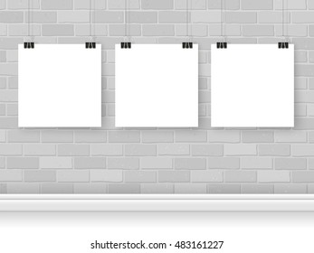 Posters on binder clips on bricks wall. Square paper mockups set. Modern trendy framing for your design. Vector template for picture, painting, drawing, quotes poster or photo.