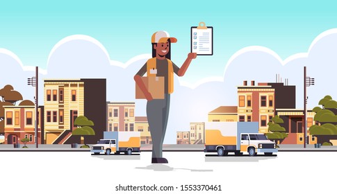 postwoman in uniform holding cardboard parcel box and receiving form african american courier express delivery service concept modern city street cityscape background flat full length horizontal