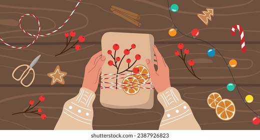 Pprocess Preparing for Winter holidays. Hands packing Christmas gift in craft paper and natural decorations on wooden table. Top view flat background. Eco friendly Xmas concept