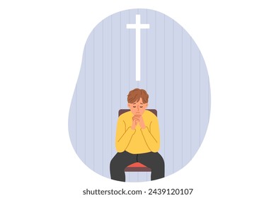 Praying teenage boy cries, sitting in church under catholic cross and prays for mother recovery. Praying teenage boy experiences grief and asks god for help, visiting christian cathedral alone
