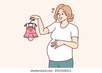 Pregnant woman with clothes for little girl in hand, dreaming birth of daughter. Pregnant lady, mother unborn child, chooses dress, imagining happy motherhood and opportunity to spend time with child