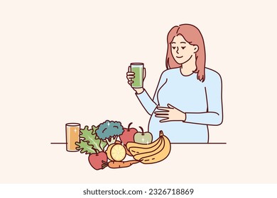 Pregnant woman drinks juice from fresh fruits and vegetables standing near steel with healthy food with vitamins. Pregnant girl is preparing to become mother and take care of unborn child