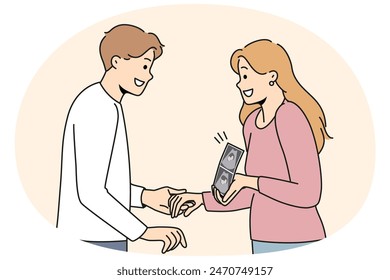 Pregnant woman holding ultrasound picture with baby showing future kiddy to happy father. Positive couple of man and girl getting ready to become parents and holding hands after going to doctor