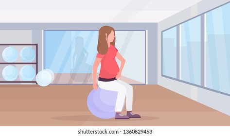 pregnant woman sitting on gymnastic ball doing yoga exercises girl working out fitness pregnancy healthy lifestyle concept modern health club studio interior horizontal